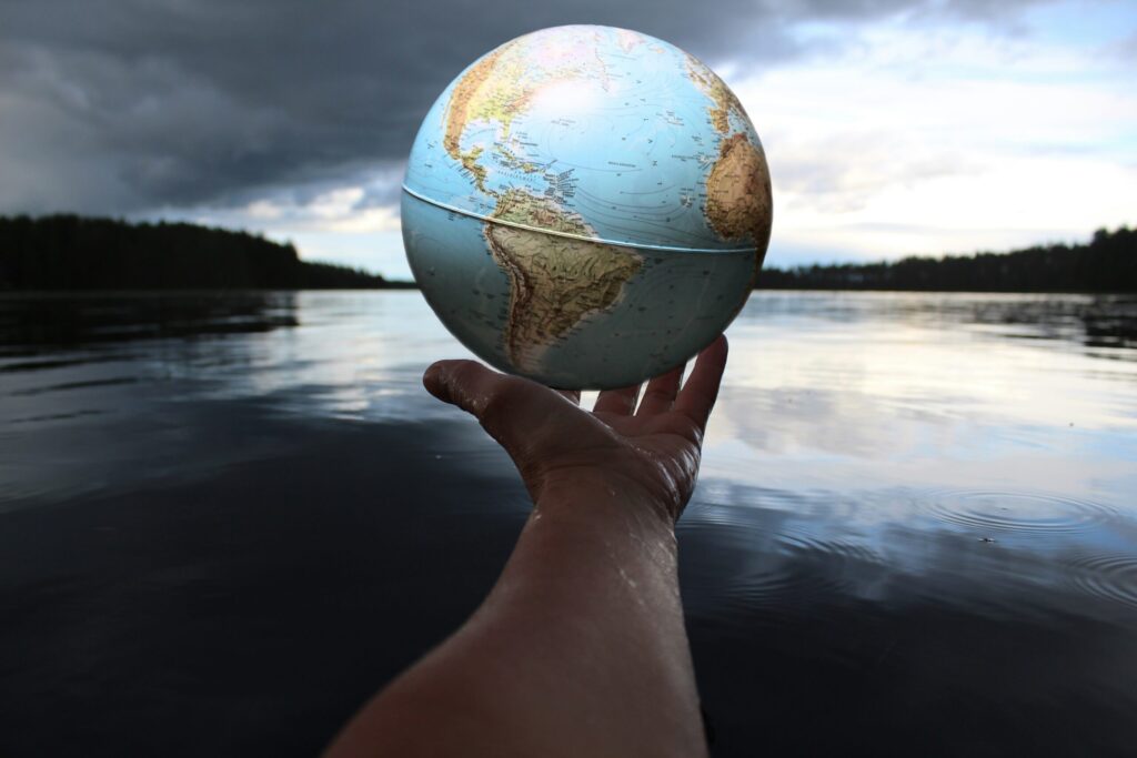 A hand holding a small globe with a lake as a backdrop.