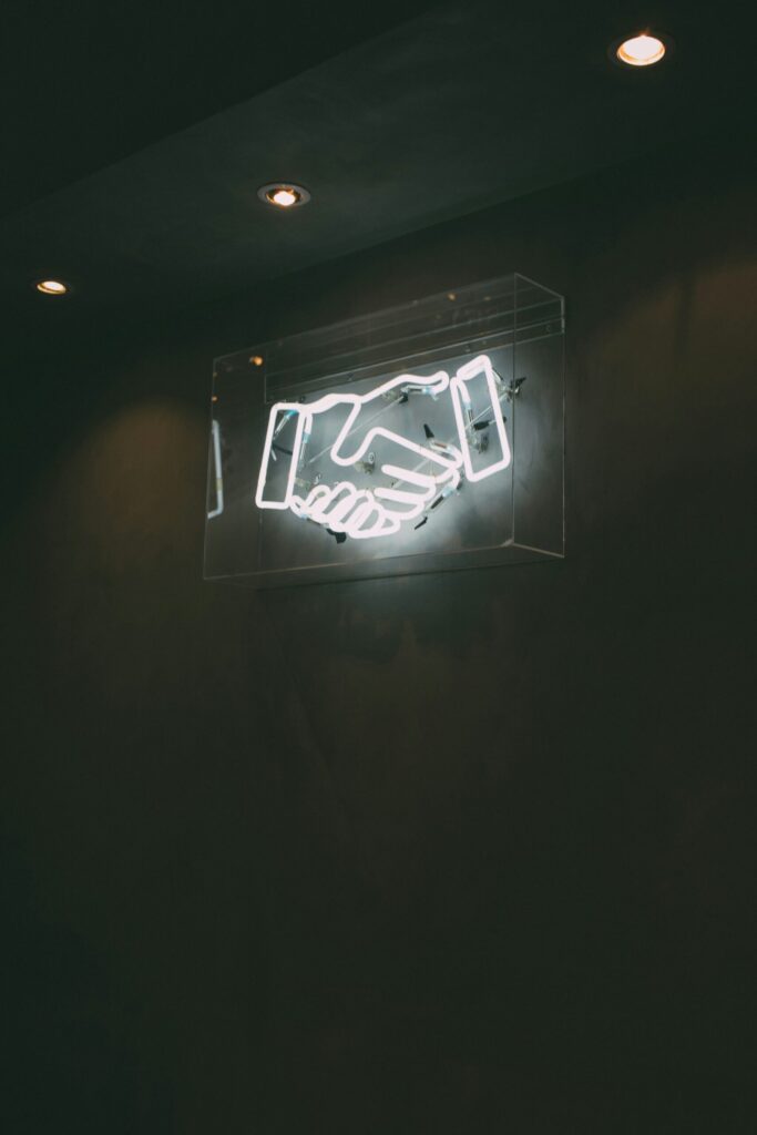 Image of a neon sign with two hands shaking.
